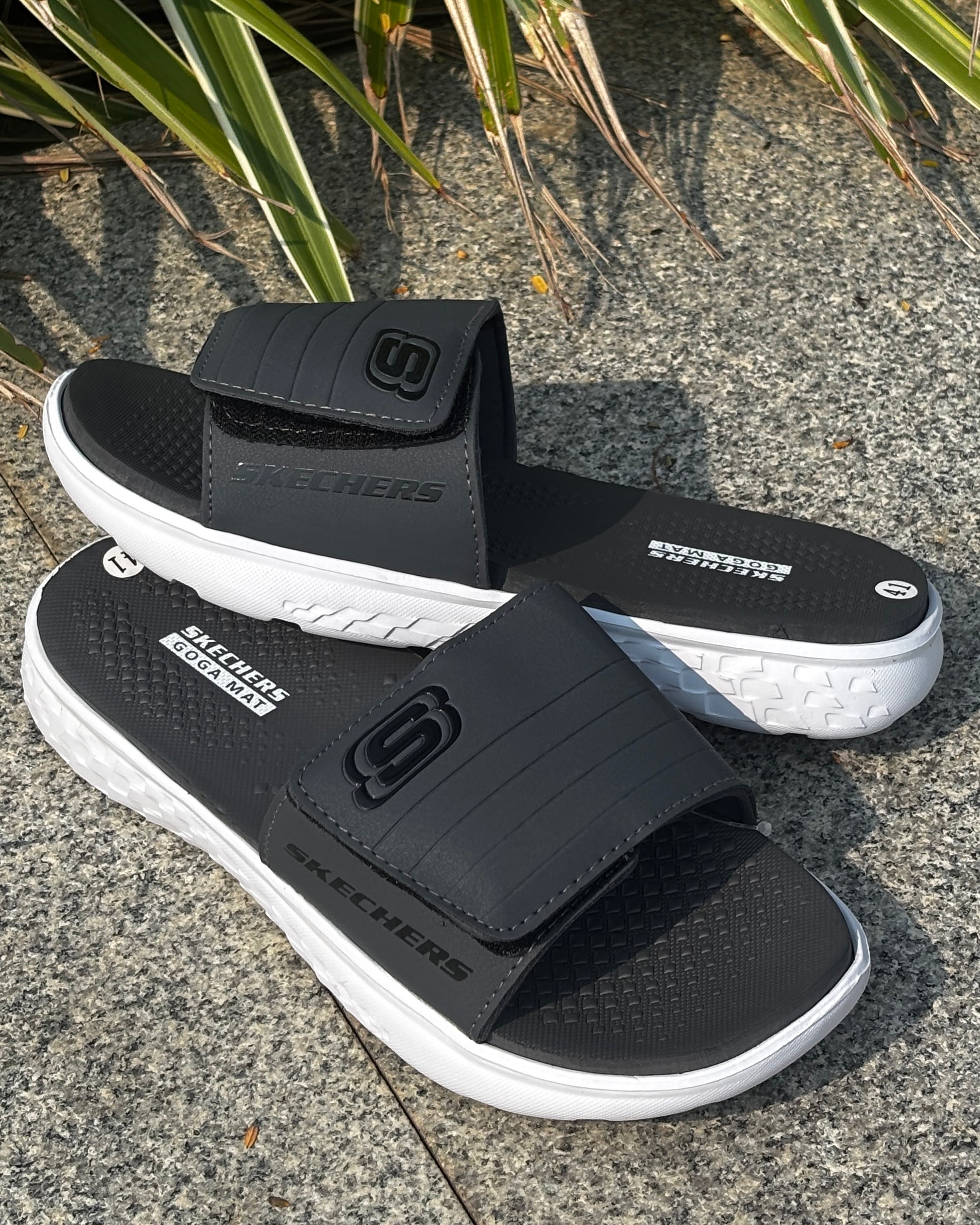 GRAY and white SKECHERS sandals on a concrete surface with grass in the background

